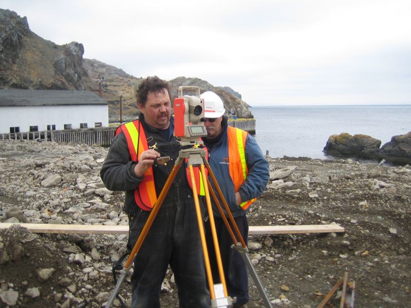 Two crew members in hi-vis vests setting up a survey instrument to mark out a basement